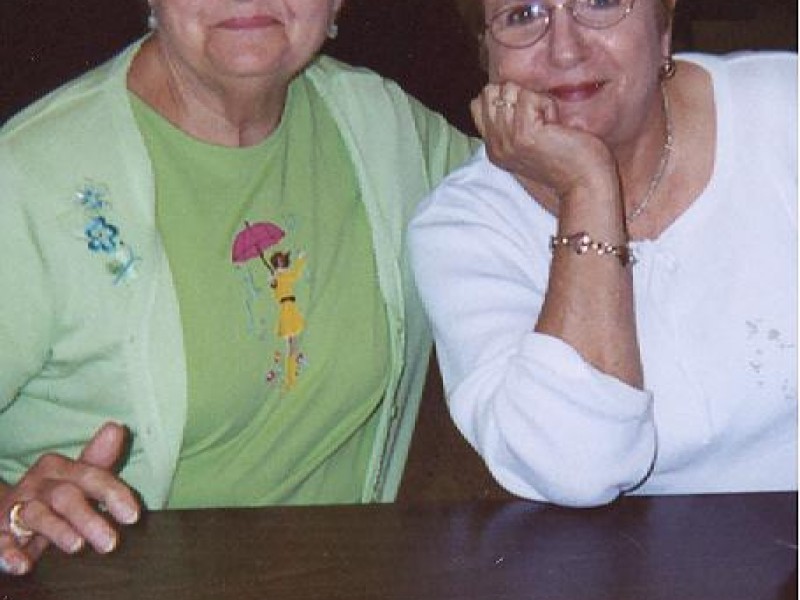two ladies smile and lean on a table
