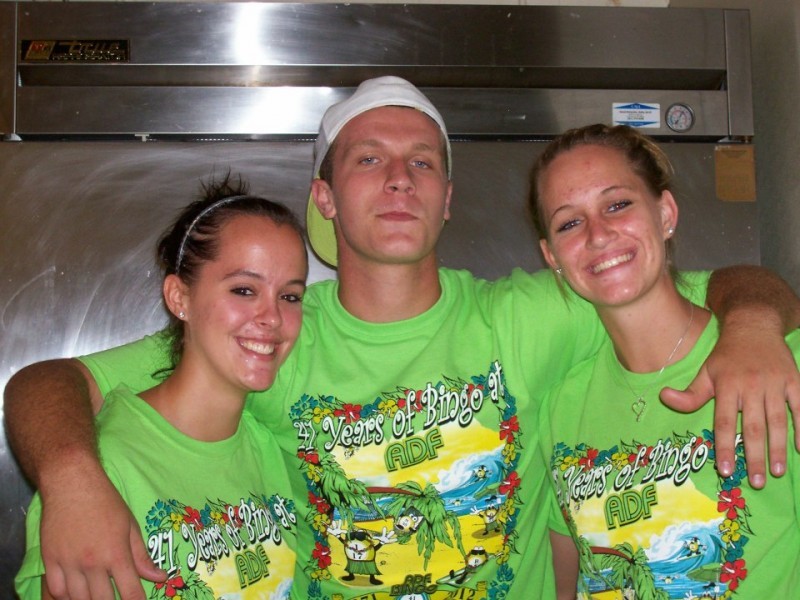 man with arms around two women all in green shirts