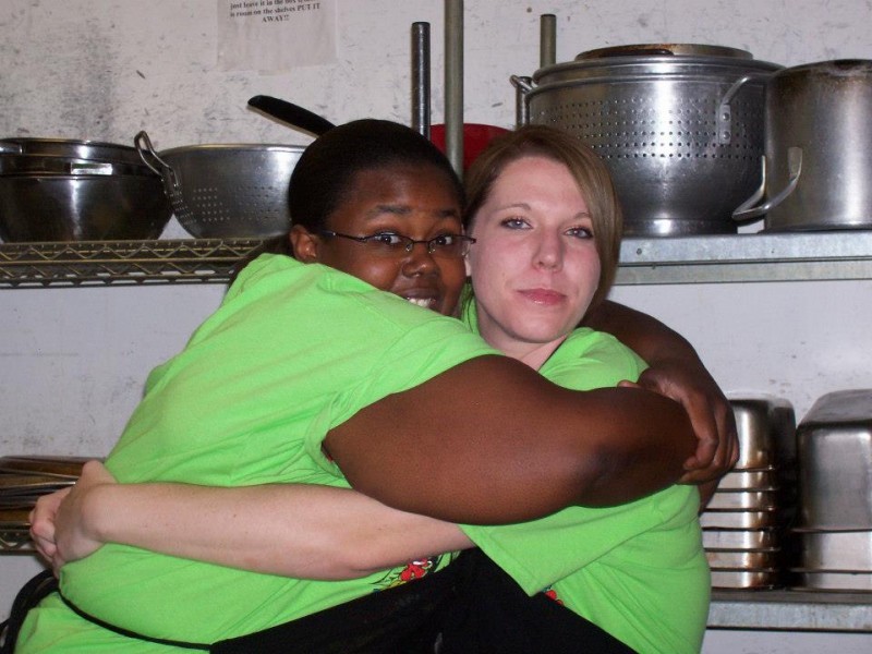 two women hug wearing green shirts hug in kitchen