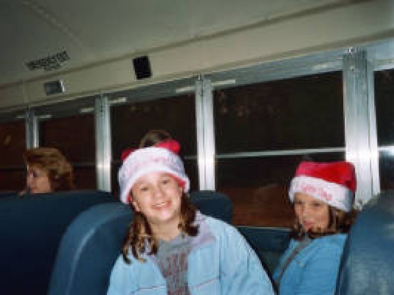 two kids pose in santa hats on a schoolbus