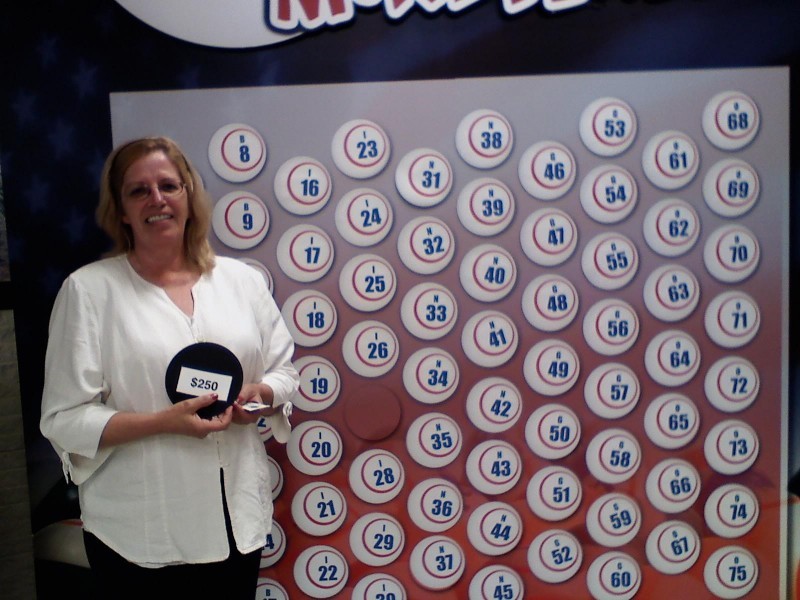 smiling woman holds a money ball winner in front of wall of money balls