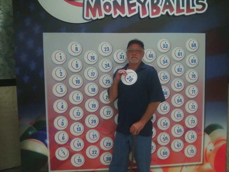 smiling man holds a money ball #28 in front of wall of money balls