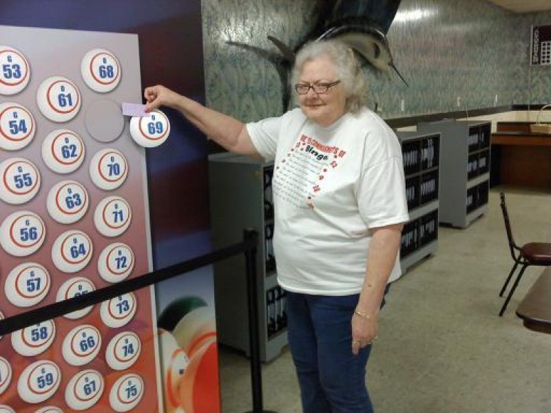 smiling woman holds a money ball #69 in front of wall of money balls