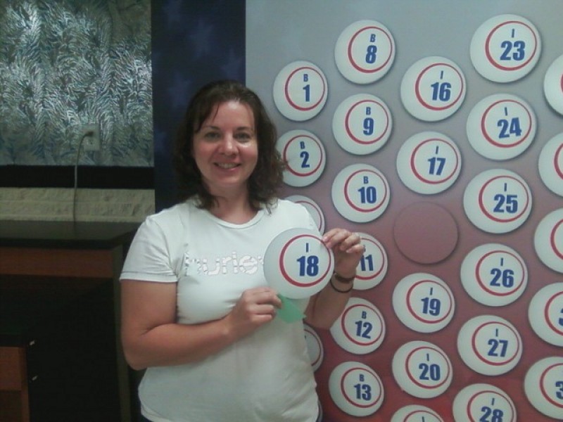 smiling woman holds a money ball #36 in front of wall of money balls