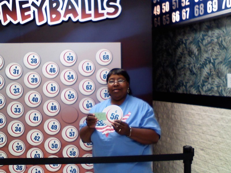 smiling woman holds a money ball #36 in front of wall of money balls