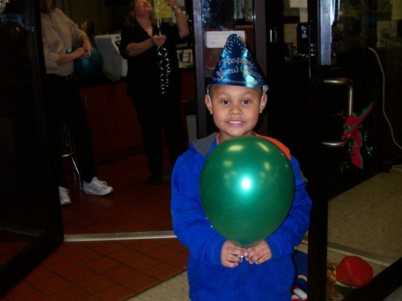 boy in party hat holds a green balloon 